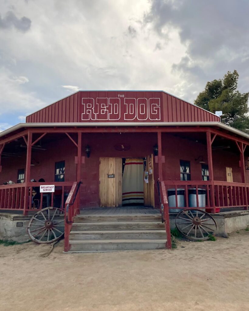 Red Dog Saloon in Pioneertown - red building with wrap-around porch and stairs up to the door with wagon wheel leaning against it