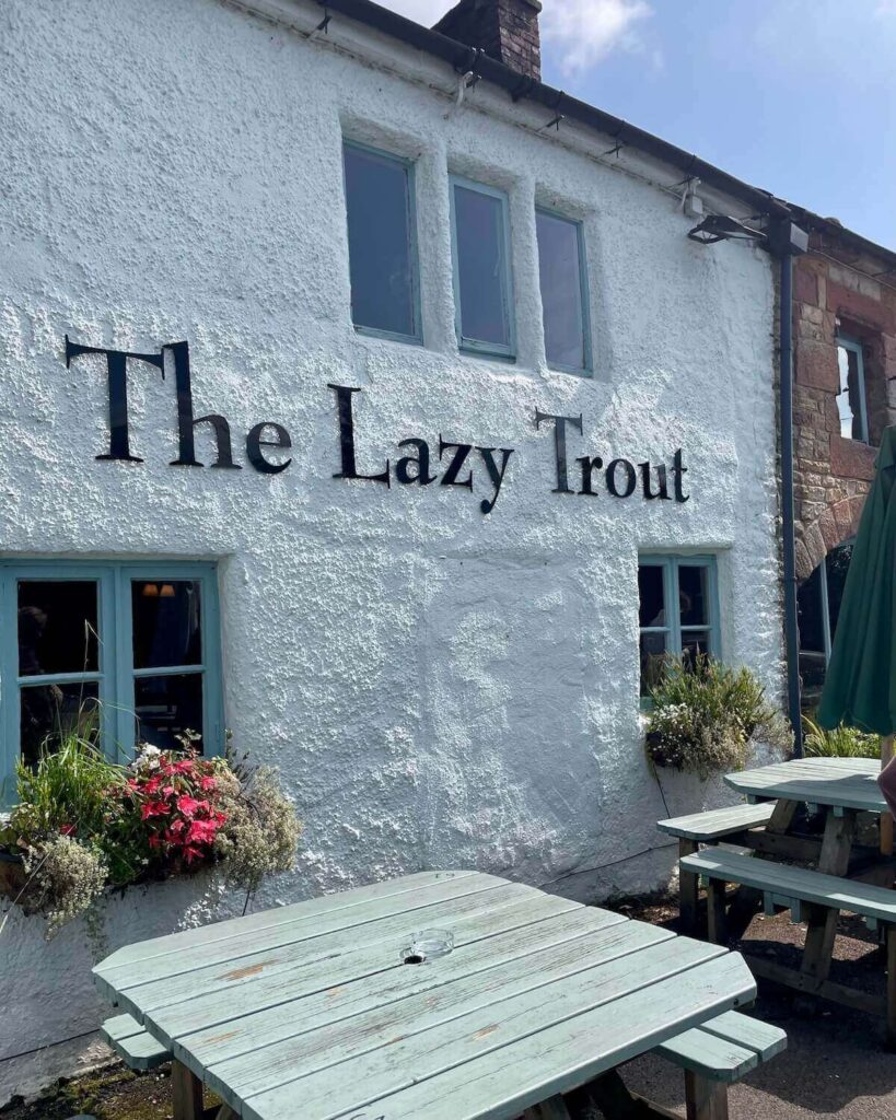 Exterior of the Lazy Trout pub covered in white paint and large name sign with picnic benches out front in Leek
