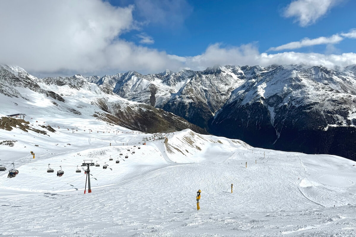 Skiing in Solden Austria - wide ski slope with chair lift along the side and huge mountain range in background on sunny day