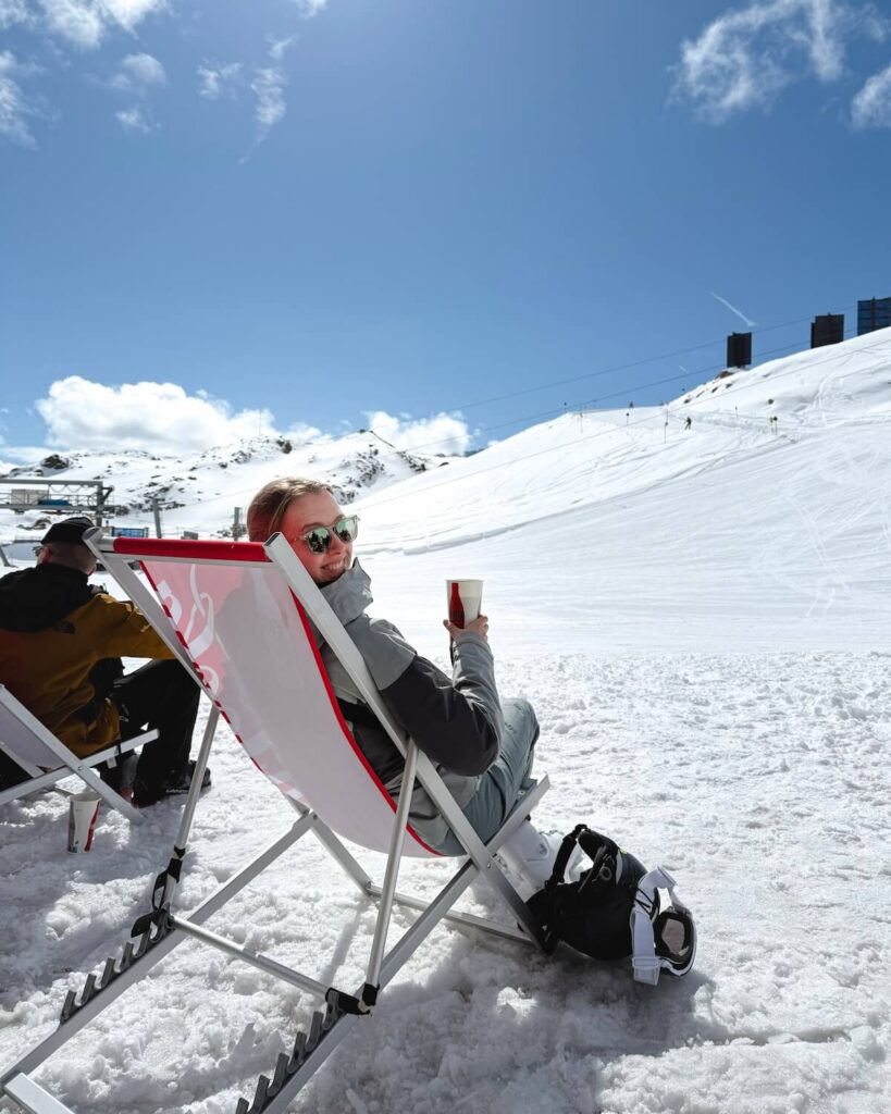 Samantha sitting in red coca cola deck chair holding a drink while at a mountain hut in the sun t Solden Ski resort