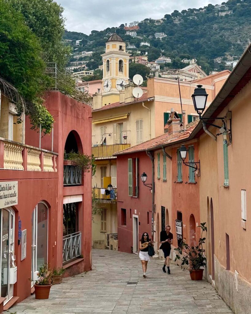 Villefranche sur mer - pastel orange and red coloured street with yellow clock tower and people walking along street