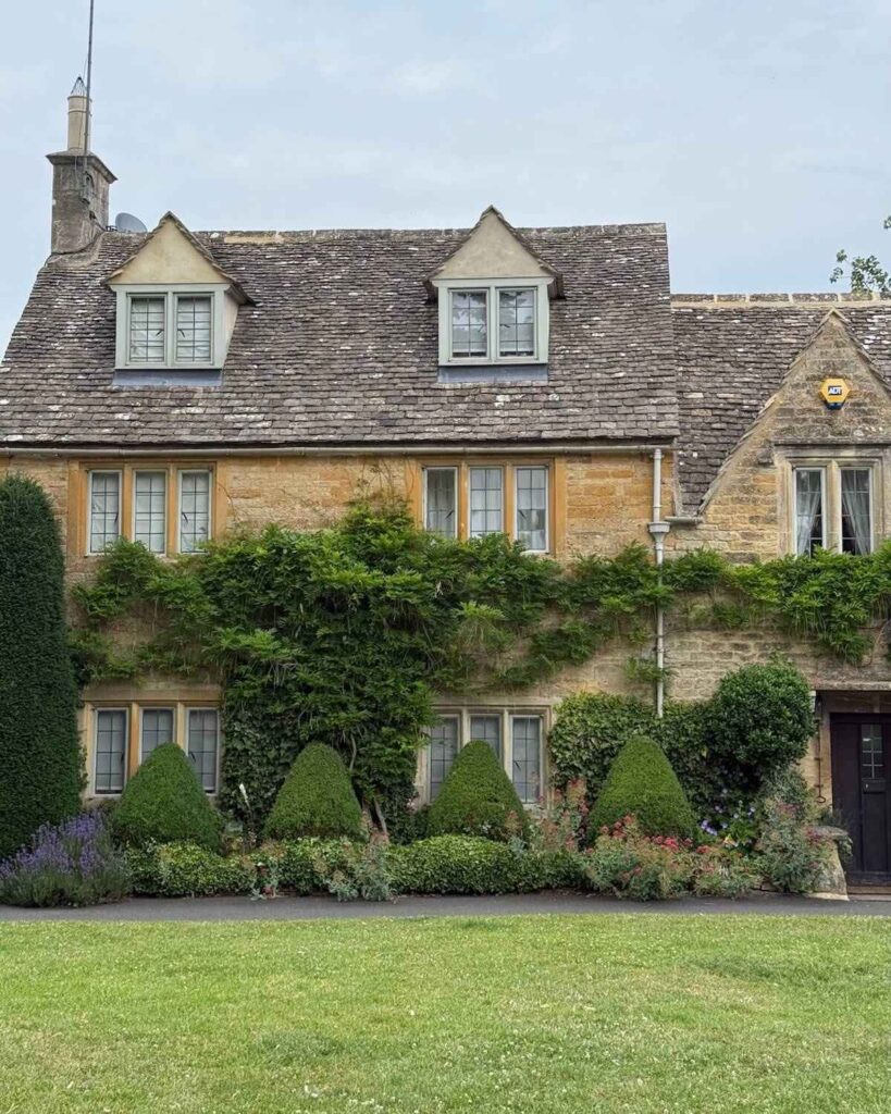 Typical cottage in Lower Slaughter in the Cotswolds - yellow brick house with manicured shrugs and flowers out front