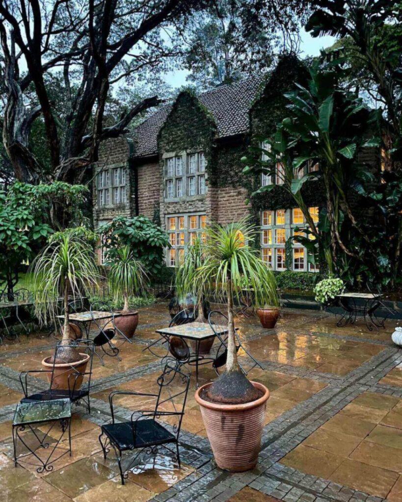 Rainy terrace at Giraffe Manor with lit up windows at Garden Manor building and garden furniture with seats tipped up