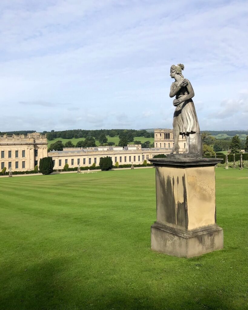 Chatsworth House in the Peak District - statue of lady on grass with large stately home in backdrop and vast countryside