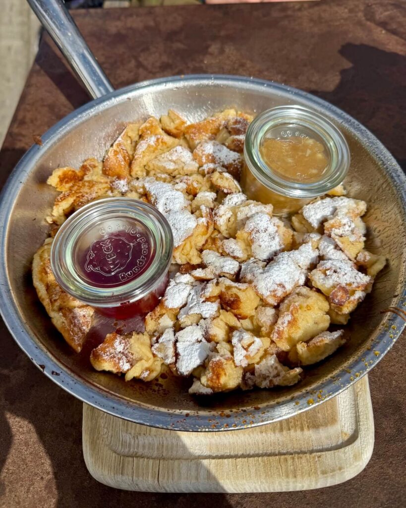 Kaiserschmarrn, sweet scrambled pancakes, in frying pan on table with pots of cranberry and apple sauce topped with powder sugar from Almwirtschaft Gampe Thaya