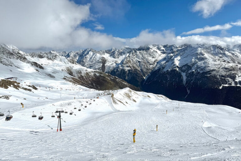 Skiing in Solden Austria - wide ski slope with chair lift along the side and huge mountain range in background on sunny day