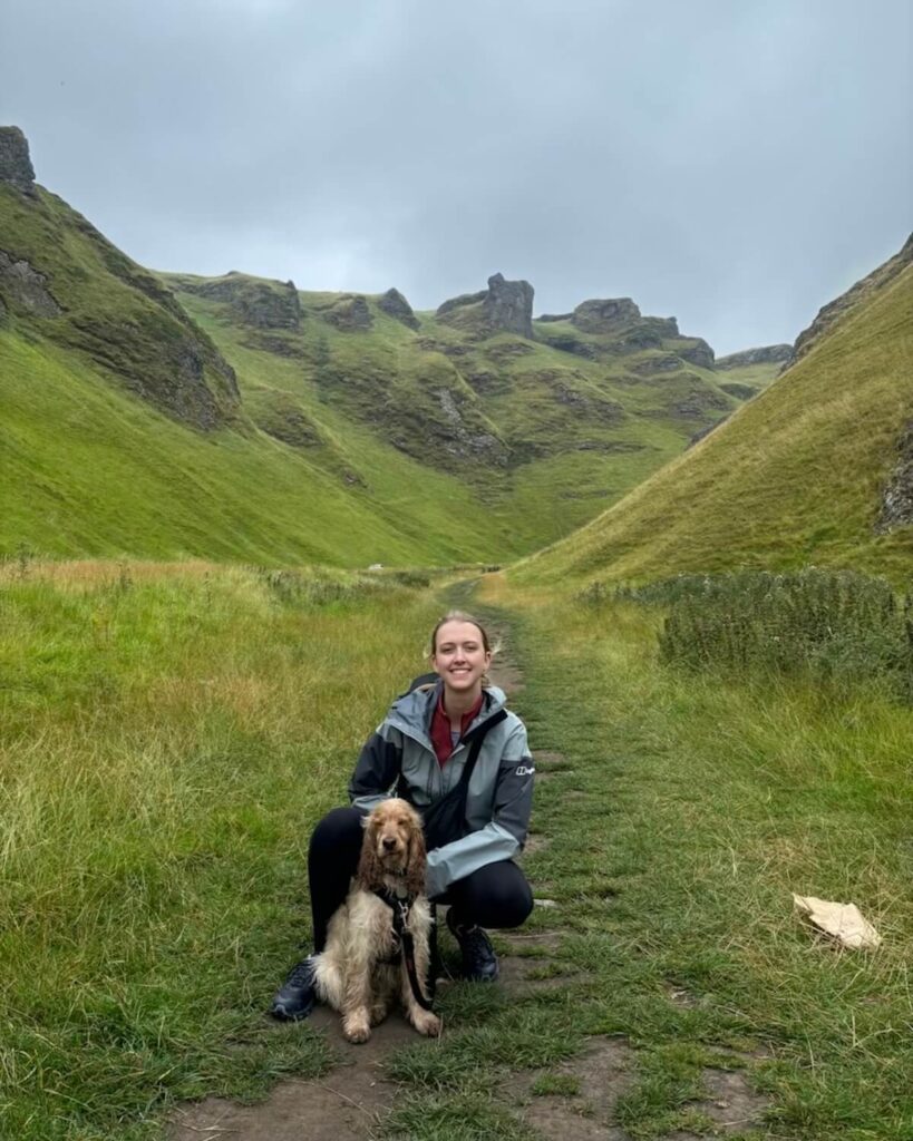 Samantha crouched down with wet cocker spaniel dog in Winnats pass with steep grass slopes and rocky cliffs on foggy day