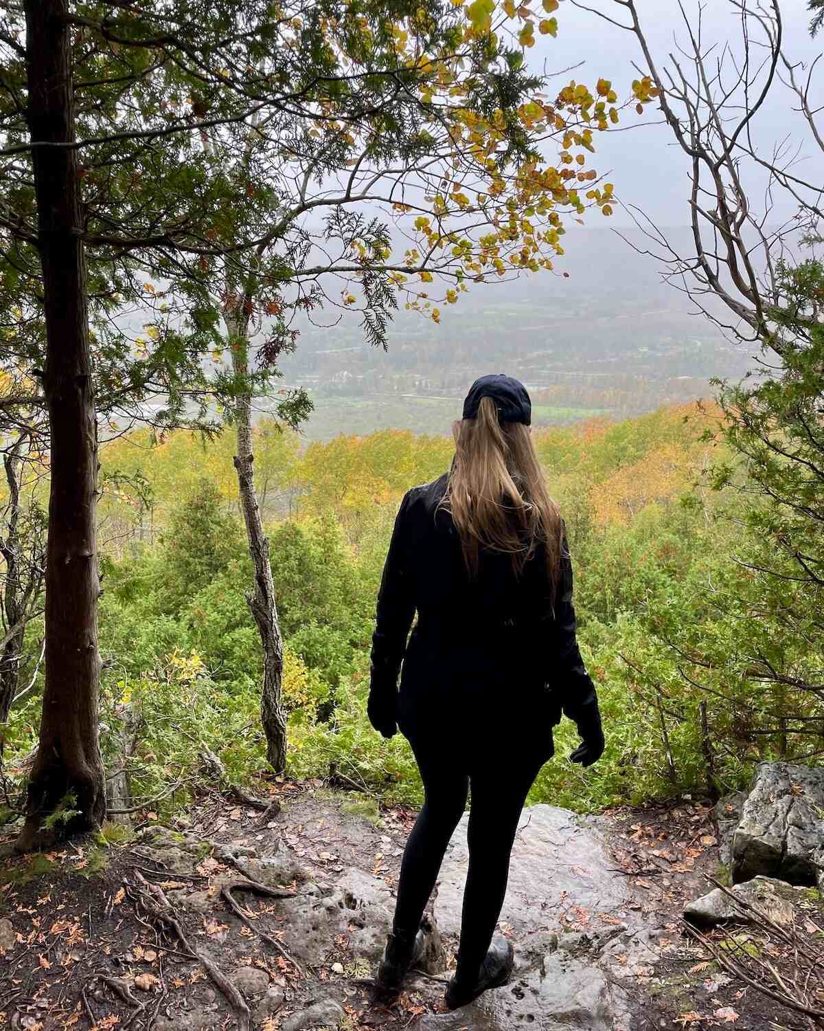 Samantha looking out at Beaver Valley on a rainy and cloudy day in autumn with colourful leaves, dressed in all black and wet
