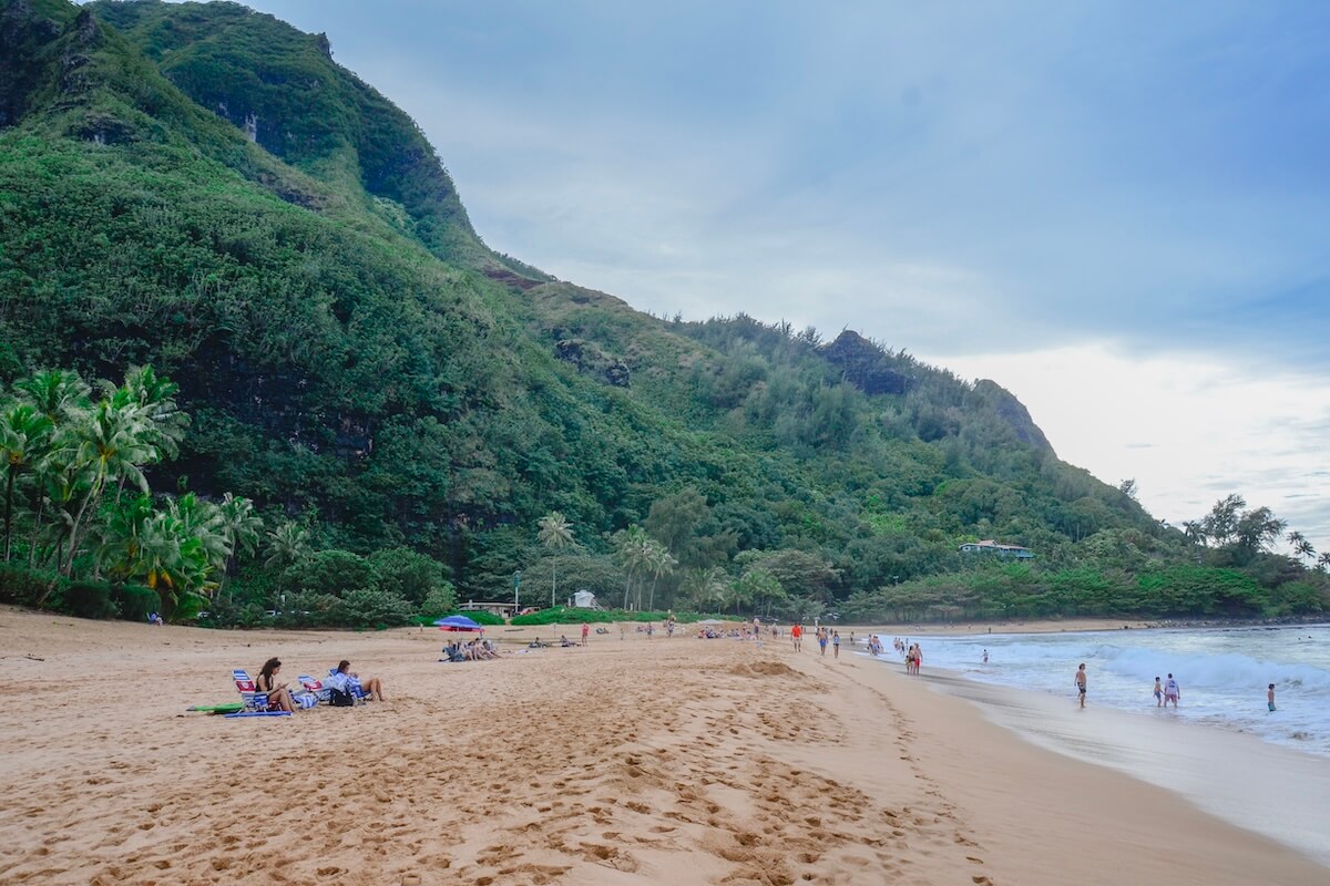 Beach in Northern Kauai with beachgoer sitting on chairs and wadding in the water with vast forest and palm trees around the edge - how many days in Kauai