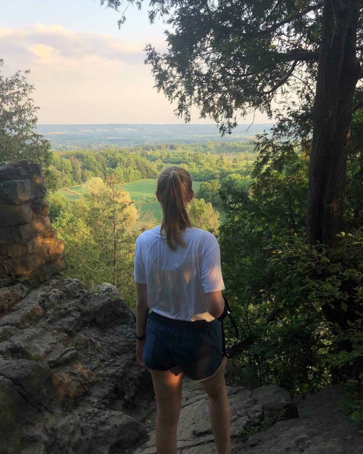 Samantha standing at lookout point at Rattlesnake Point overlooking trees as far as the eye can see with golden hour lighting